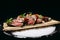 Hot appetizer Veal Tataki on a wooden tray on a black background