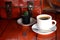 Hot Black Americano coffee in white cup with vintage brown leather bag on teak wooden background