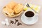 Hot black coffee, wicker basket with flaky biscuits, sugar cubes