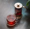 Hot black tea with steam over it in a Cup and a glass copper teapot next to it on a wooden table