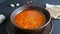 Hot boiled red tomato soup with corn with steam in a brown clay plate in a rustic style