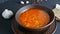 Hot boiled red tomato soup with corn with steam in a brown clay plate in a rustic style