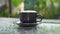 Hot cappuccino coffee cup on grass table in garden with dewdrop