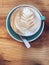 Hot Cappuccino coffee decorated with Tree Leaves on Milk Latte Foam Froth art in blue mug cup on rustic wooden table background.