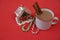 Hot chocolate cocoa in a mug with cinnamon and gingerbread house candy sweet canes on a red background with copy space for text.