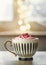 Hot chocolate with pink whipped cream and sprinkles in cup on table at window background with bokeh. Cozy time at home with