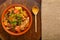 hot cholent sprinkled with green onions on a wooden stand with a wooden spoon on a set Shabbat table.