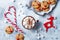 Hot cocoa with marshmallow in ceramic mug surrounded by Christmas gingerbread. Decorated red nosed reindeer cookies.