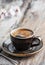 Hot coffee in a black cup, vintage wooden background style. Spring branches of white flowers of cherry near. Close up