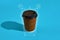 Hot coffee in brown paper cup with black lid on blue background