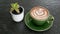 Hot coffee cappuccino latte art in jade color cup on black stone table background with cactus plant