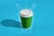 Hot coffee in green paper cup with white lid on blue background