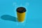 Hot coffee in yellow paper cup with black lid on blue background