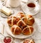 Hot cross buns, freshly baked hot cross buns on a white plate and fresh butter and rose jam on a wooden table, top view.