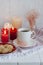 A hot cup of black tea with homemade cookies on a striped tablecloth, wax candles, a glass vase with decorative herbs on a white