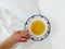 Hot cup of green tea in white decorative china cup held by hand on white background. flat lay. top view.