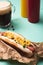 Hot dog with corn, glass of beer and bottles with mustard and ketchup on blue.