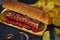 Hot dog -Hot sausage nested in a bun with cucumbers, red pepper and onions. On a dark background with chips. Fast food concept