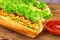 Hot dog with sausage, lettuce, tomato, cucumber, ketchup and mustard on wooden background.