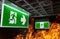 Hot flame fire and green fire escape sign hang on the ceiling in the office at night. The concept of fire escape training and