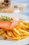 Hot french fries with salmon served on plate with lemon