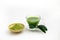 Hot fresh Green Tea drink in through white glass cup and dish. Place with deep green tea leaves and extract powder in wooden bowl.
