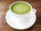 Hot green tea matcha latte cup with white saucer on wood texture