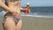 Hot lady standing on seaside beach, putting skincare spray on legs, belly, body