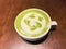 Hot matcha green tea milk latte with creamy milk is flower or plant pattern, a little sugar and teaspoon in a cup on the wooden