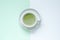 hot matcha latte in round white ceramic mug on white ceramic saucer placed on two colour of white  and light green background.