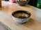 Hot miso soup with cut egg in golden broth with sesame seeds in black and white plate on table. Top view. Dish of Japanese cuisine