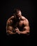 Hot muscular man on a black background. A shirtless bodybuilder showing off triceps and biceps. Hard workout concept.