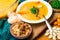 hot pumpkin soup in glass pan and in white plate, decorated with mini carrot, pumpkin seeds, mushroom, honey agaric and green kelp