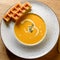 Hot pumpkin soup in white bowl with Belgian waffles. View from above, macro view