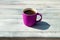 Hot purple cup of black coffee on rustic wooden bright table. Outdoor in the afternoon.