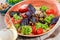 Hot salad with grilled tomatoes, eggplant, zucchini, red pepper, salad leaves, garnished with grated walnuts and basil and glass o