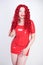 Hot sexual redheaded girl with plus size body wears fashion latex rubber red dress and posing on white studio background alone. ch