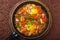 hot shakshuka in a frying pan sprinkled with green onions on a wooden stand.