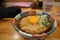 Hot soba with deep fried egg with onion in Japanese bowl on timber table