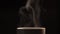 The hot tea or coffee that is pouring into the white cup has white smoke and steam effect on the black background