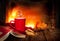 Hot tea or coffee in a red mug, book and fireplace