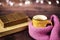Hot tea, hot chocolate, coffee in yellow cup, wrapped with a pink knitted scarf. Old books. Blurred lights, wooden background