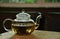 hot tea with tea leaves in glass teapot with ceramic cup on wood plate on glass table with selective focus on