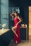 Hot young adult proud woman wearing a long scarlet red long dress sexually demonstrates her naked graceful leg, standing