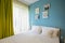 Hotel bedroom with blue walls, white sheers, pillowcases and sheets. Green curtains