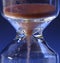 Hour Glass with running sand inside, on blue background. Time passing or countdown concept