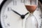 Hourglass on the background of office watch as time passing concept for business deadline, urgency and running out of time. Sand