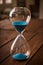 Hourglass containing blue sand on a rustic wooden board