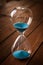 Hourglass containing blue sand on a rustic wooden board