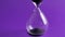 Hourglass Countdown Sand falls in a glass flask on violet 4k